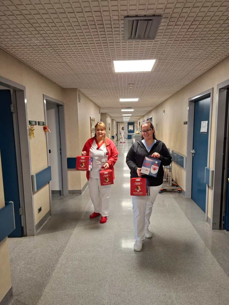 Immagine di  due infermiere sorridenti che tengono in mano i panettoni della Fondazione IEO-MONZINO mentre vanno a consegnarli ai pazienti dell'ospedale